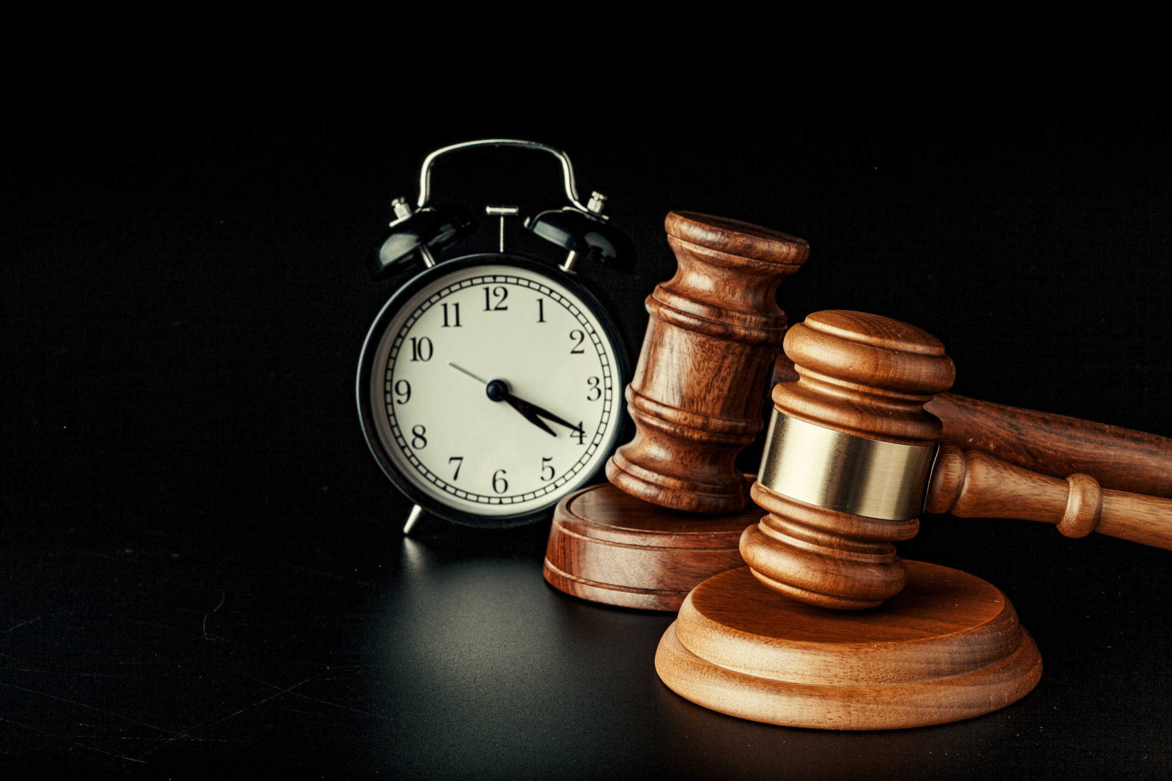 Wooden judge hammer with alarm clock on black background