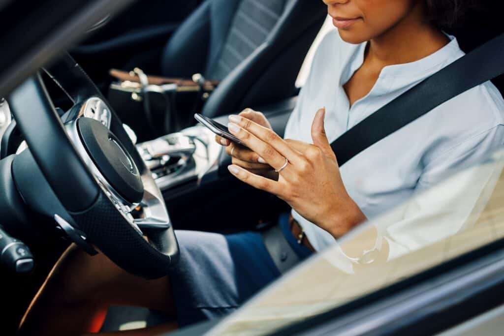 closeup of a woman in the drivers seat of a car texting while driving