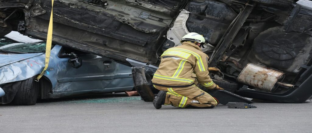 Picture of truck rolled over on top of car with firefighter nearby associated with blog on truck accidents identifying motor carriers